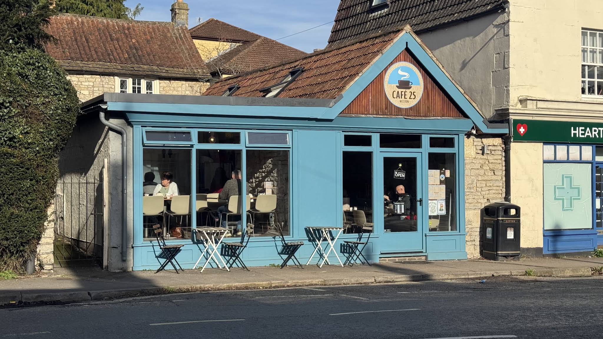 The complete sky-blue Cafe 25 Weston shopfront, with its round café sign and entrance on the right.